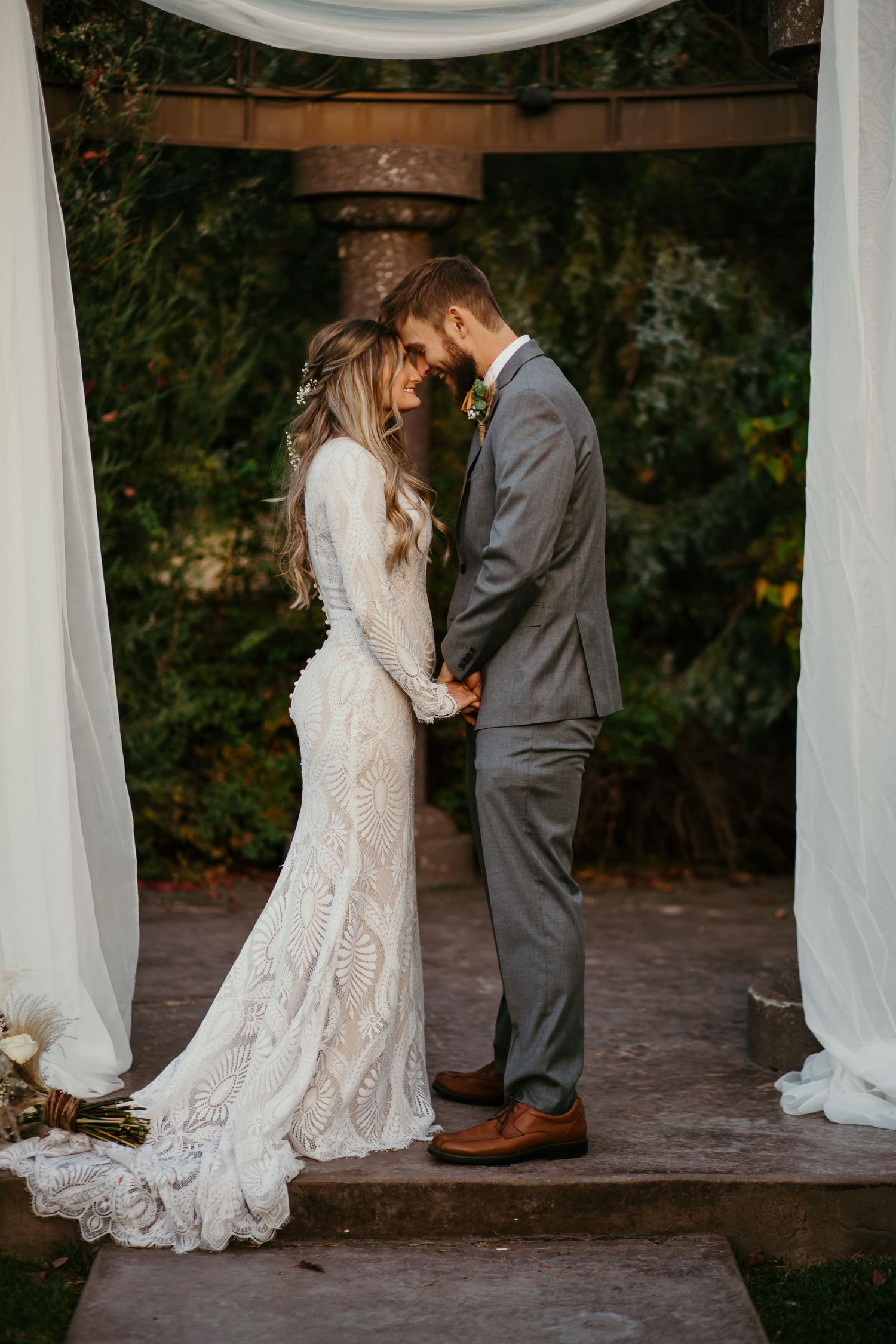 Wedding couple sharing intimate moment under draped arch during ceremony.