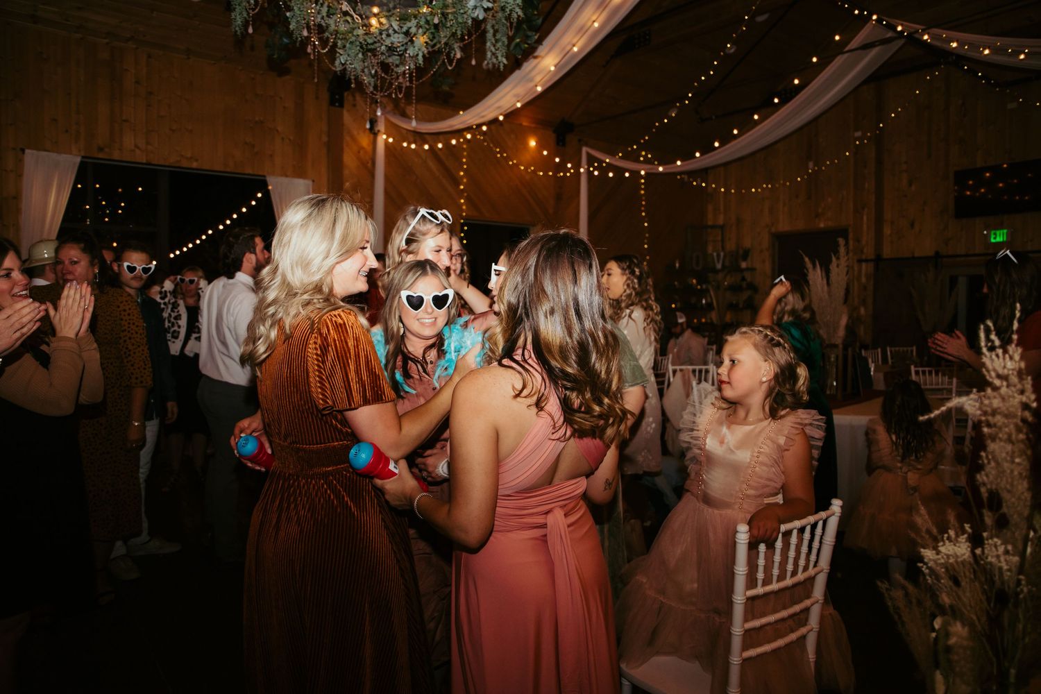 Wedding reception dance party with guests celebrating under string lights and chandelier.