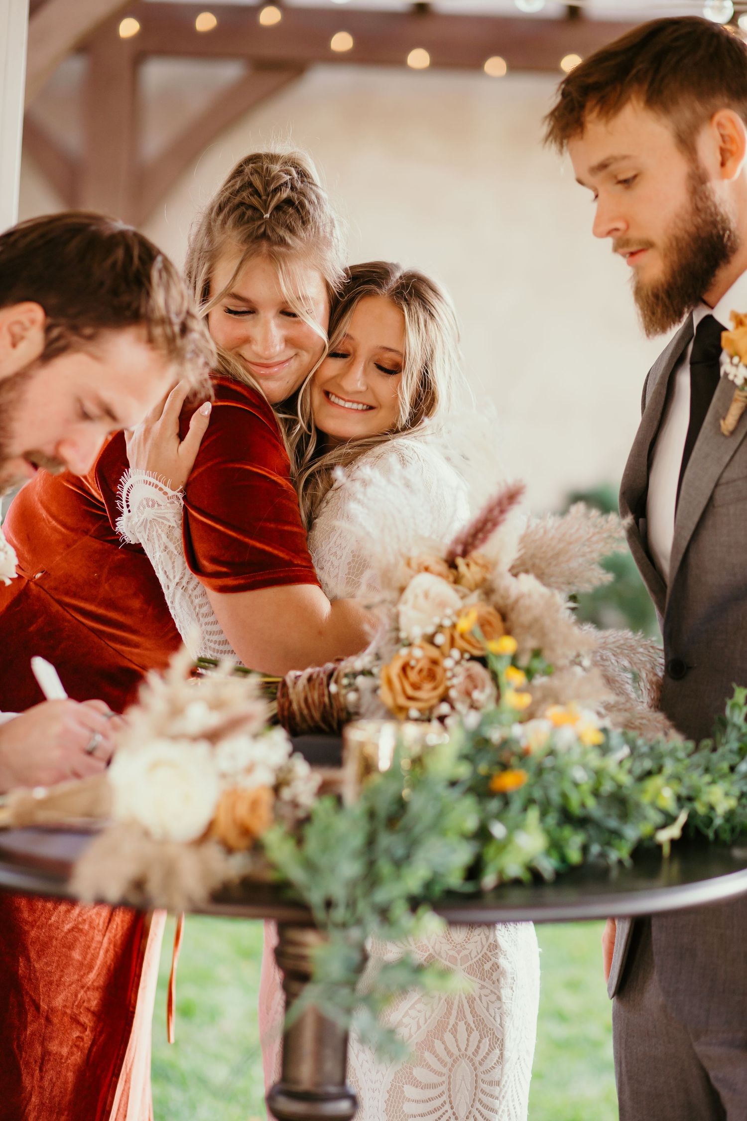 Wedding party gathers around floral display sharing laughter during reception celebration.