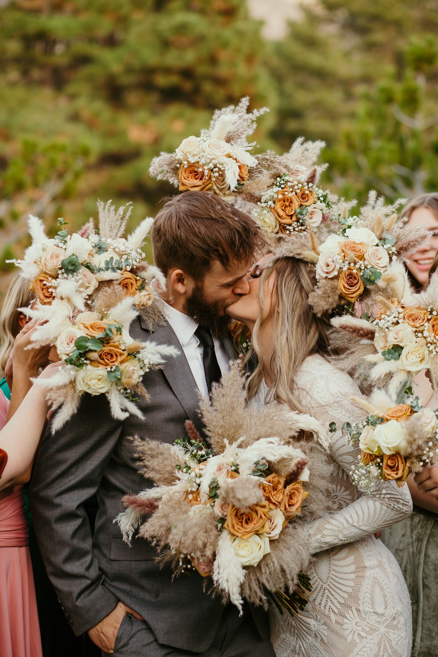 Newlyweds share romantic kiss surrounded by bridesmaids holding matching bohemian bouquets.