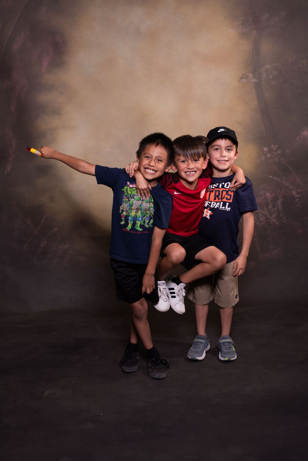 Three children posing playfully together for a studio portrait against a dark background.