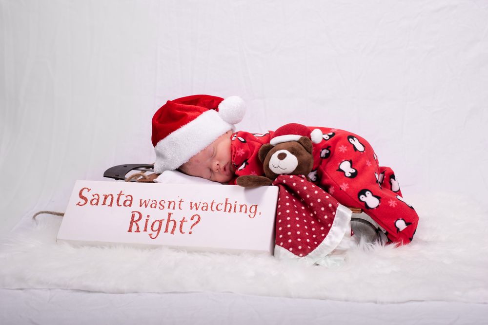 Christmas themed newborn photo setup with Santa text and holiday decorations.