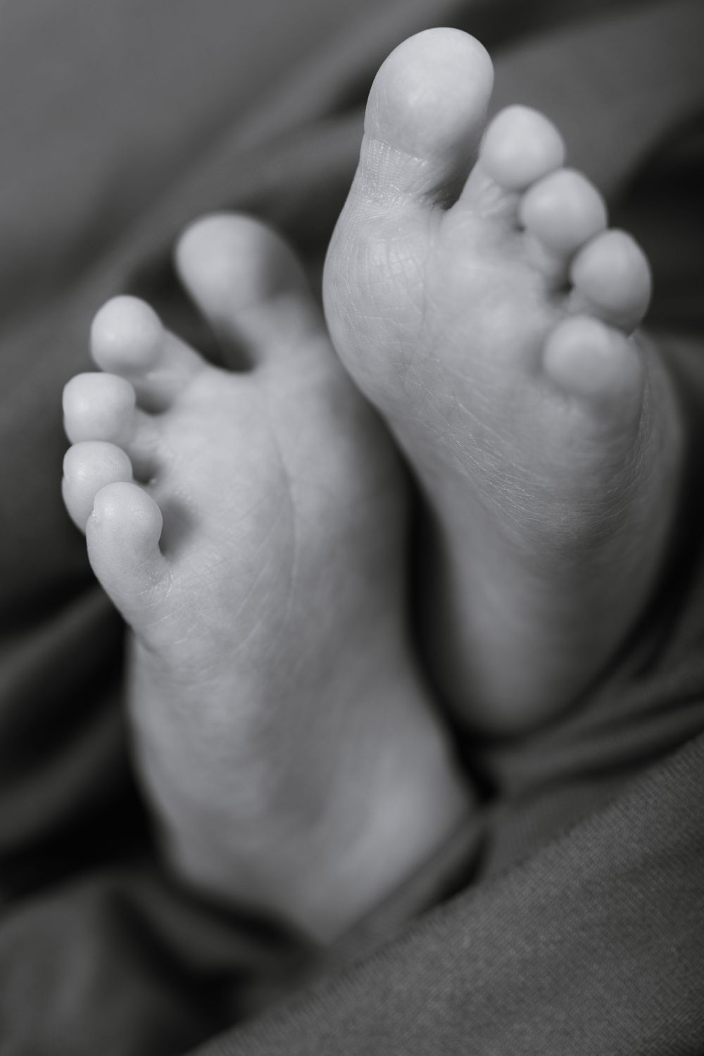 Close-up black and white photograph of tiny baby feet showing delicate toes against a dark background.