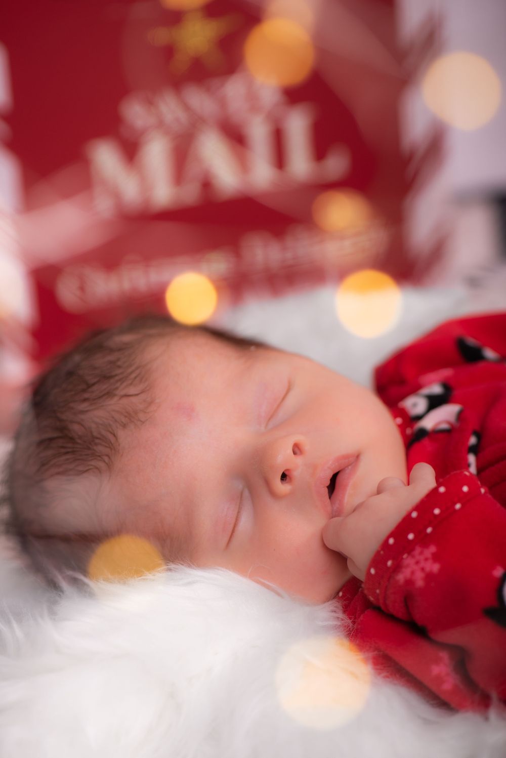 Sleeping newborn with Christmas themed decorations and soft bokeh lights.