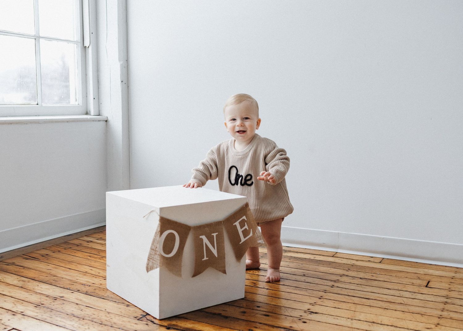 Messy cake smash photo of excited baby under ONE banner decoration.