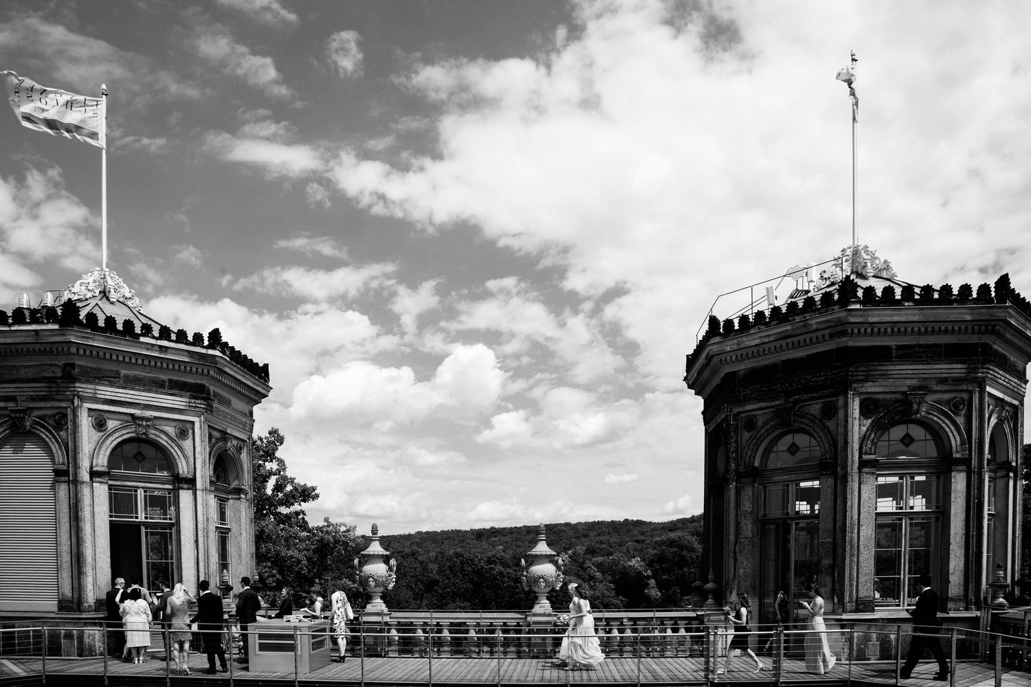 Black and white architectural photograph of two ornate Victorian pavilions with flagpoles on a terrace under cloudy skies.