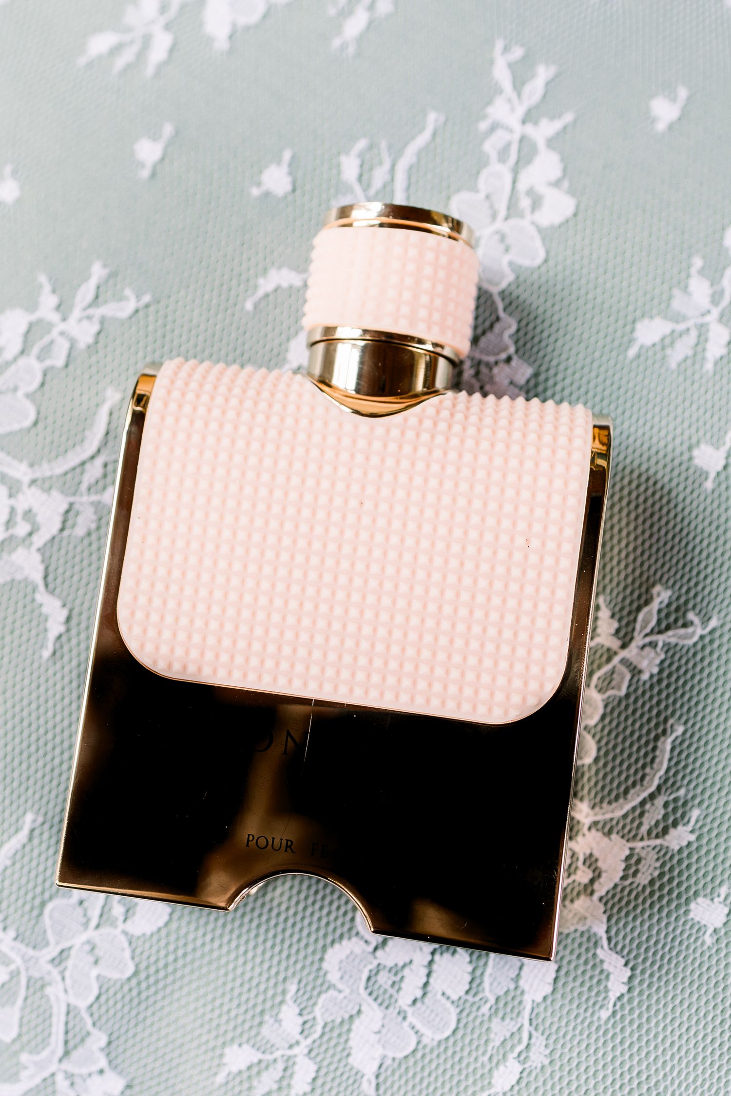 Blush pink perfume bottle with gold accents against a light floral background.