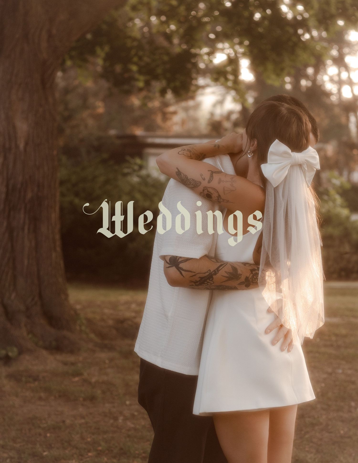 Groom is holding bride tightly as the sun pours through her veil in front of trees in Hamilton.