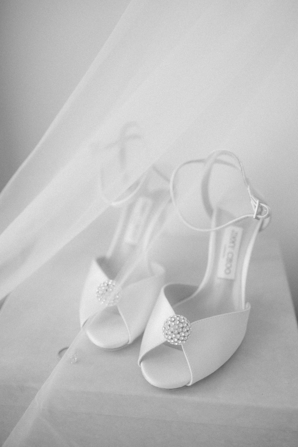 White bridal shoes with crystal embellishments photographed through delicate veil.