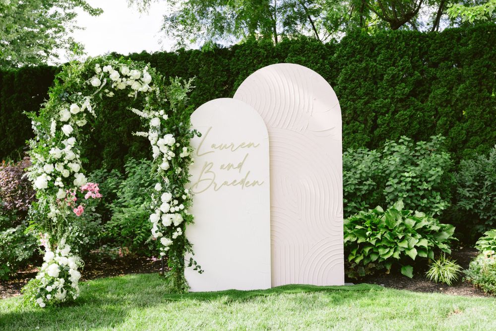 White arched wedding backdrop decorated with fresh floral arrangements in a garden setting.