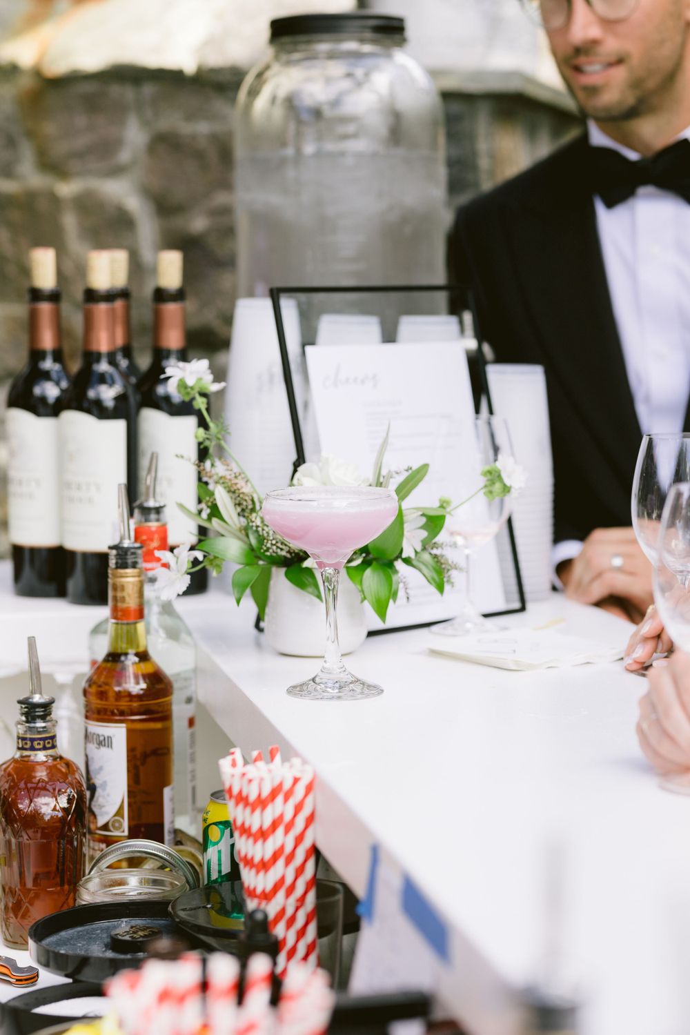 Elegant cocktail bar setup with pink drinks, wine bottles and striped straws at a formal event.