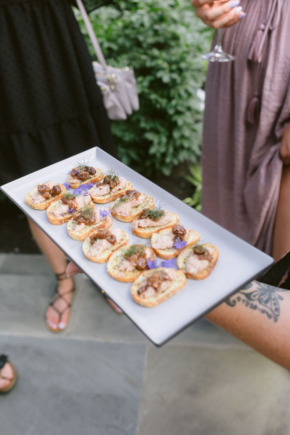 Tray of gourmet appetizers being served at an outdoor celebration.