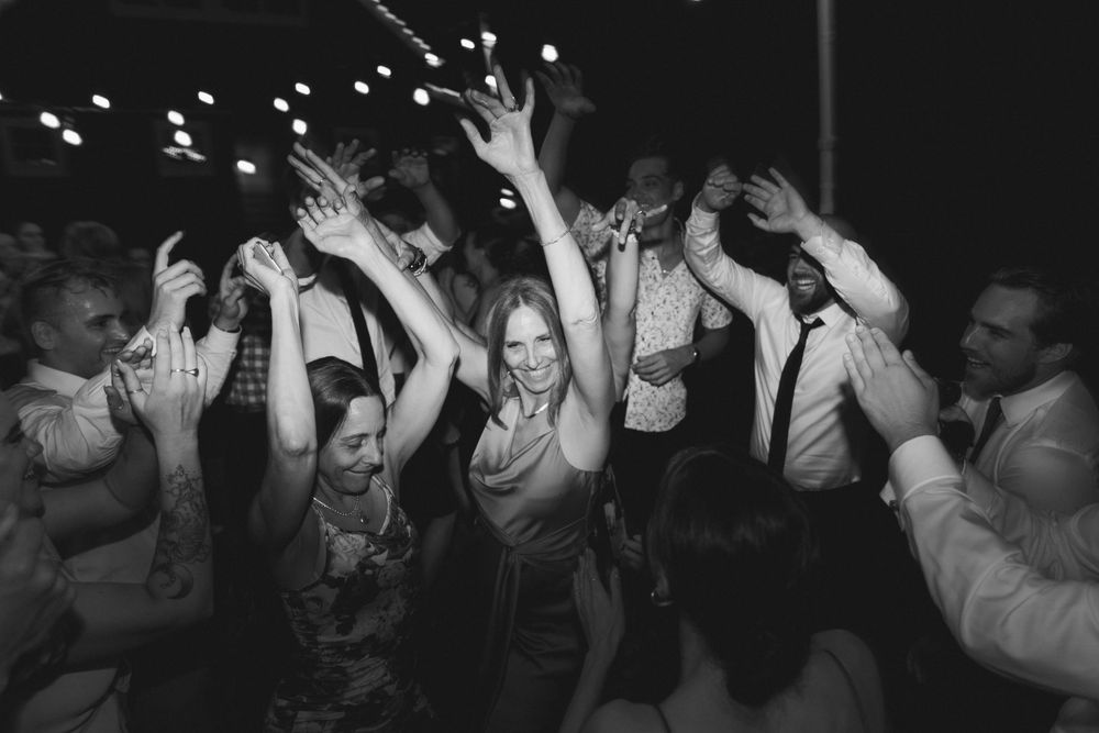 Black and white photo of people dancing with their hands raised at a lively party celebration.