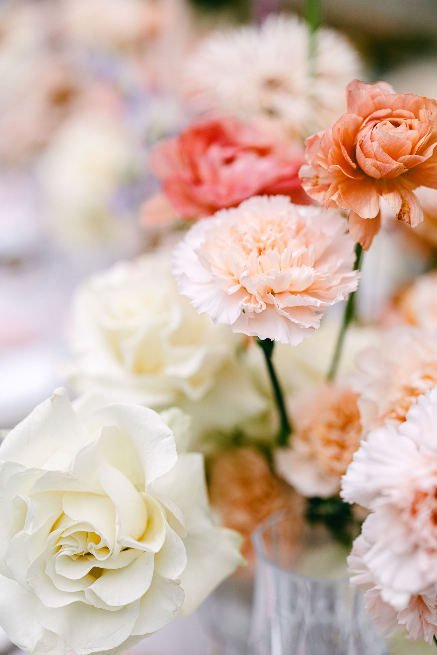 A delicate floral arrangement featuring peach and white roses and carnations in soft focus.