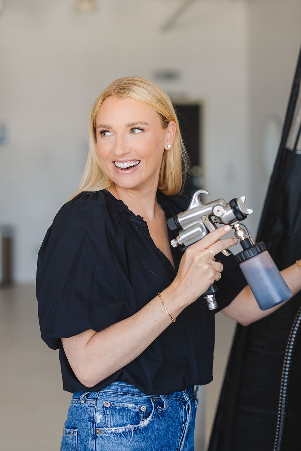 A person in a black shirt and jeans laughs while holding a camera in a studio photography sequence.