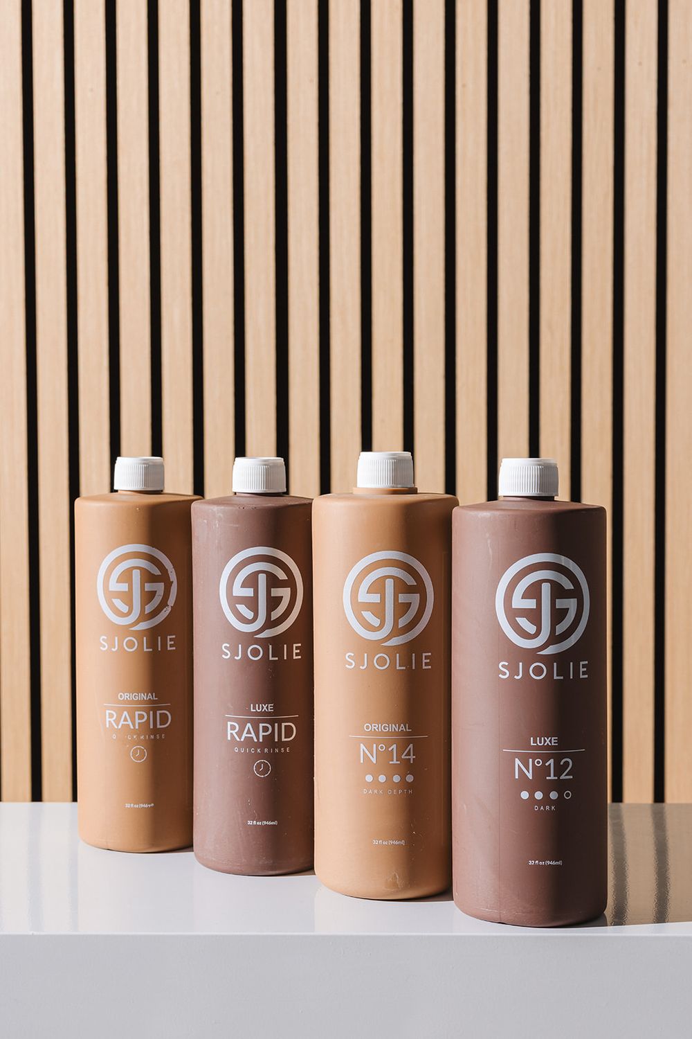 A row of minimalist brown and beige cosmetic bottles featuring the Sjolie brand name arranged against a striped backdrop.
