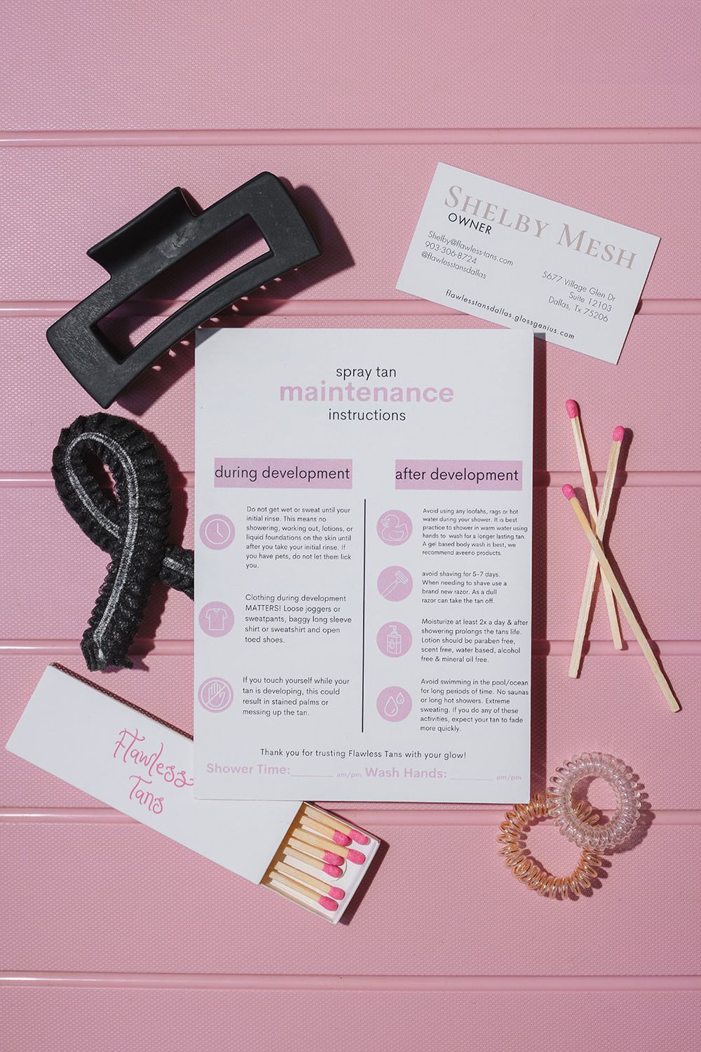 Business development instructions and accessories arranged on pink surface with black hair scrunchie and wooden sticks.