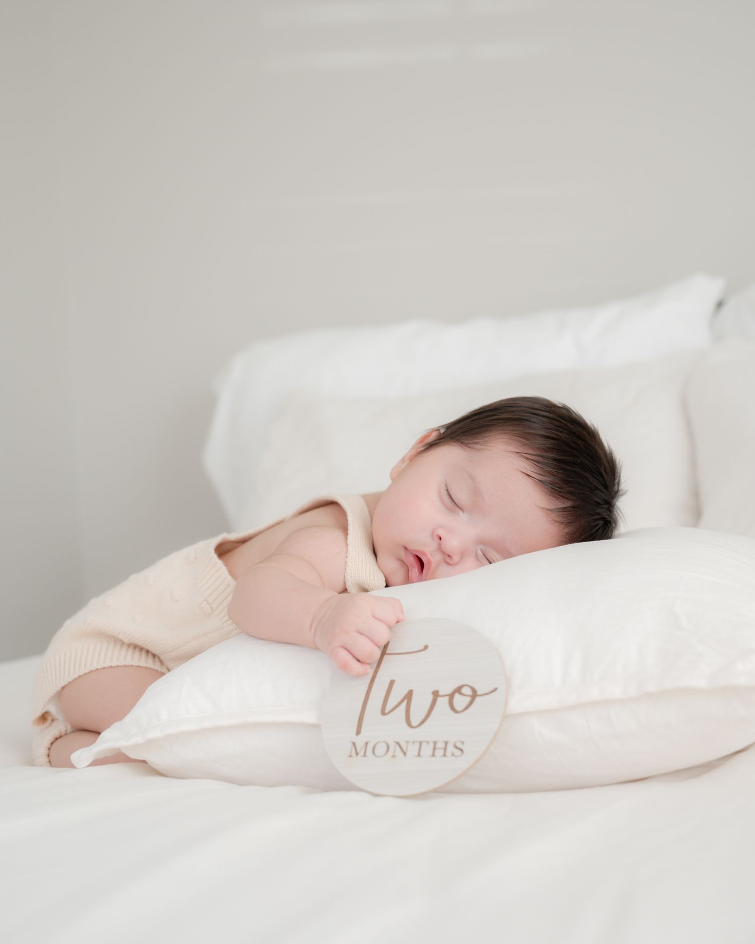 Sleeping baby rests on pillow marked 'Two months' in peaceful nursery setting.