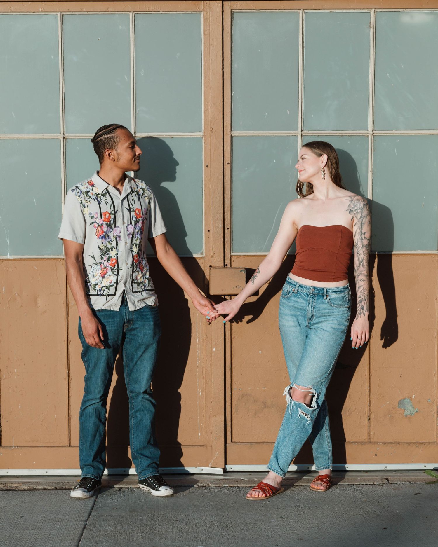 Couple holding hands against a blue wall with windows casting shadows.