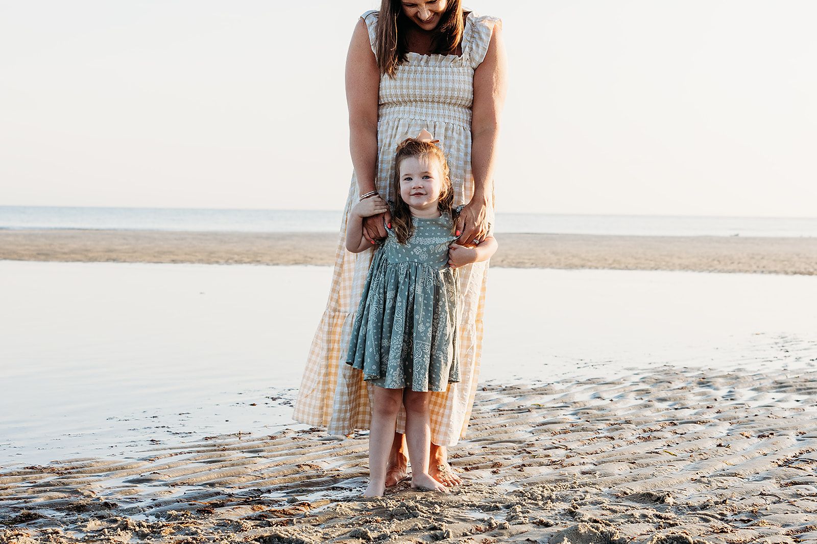 Two people stand on a sandy beach at sunset wearing coordinated outfits in soft tones.