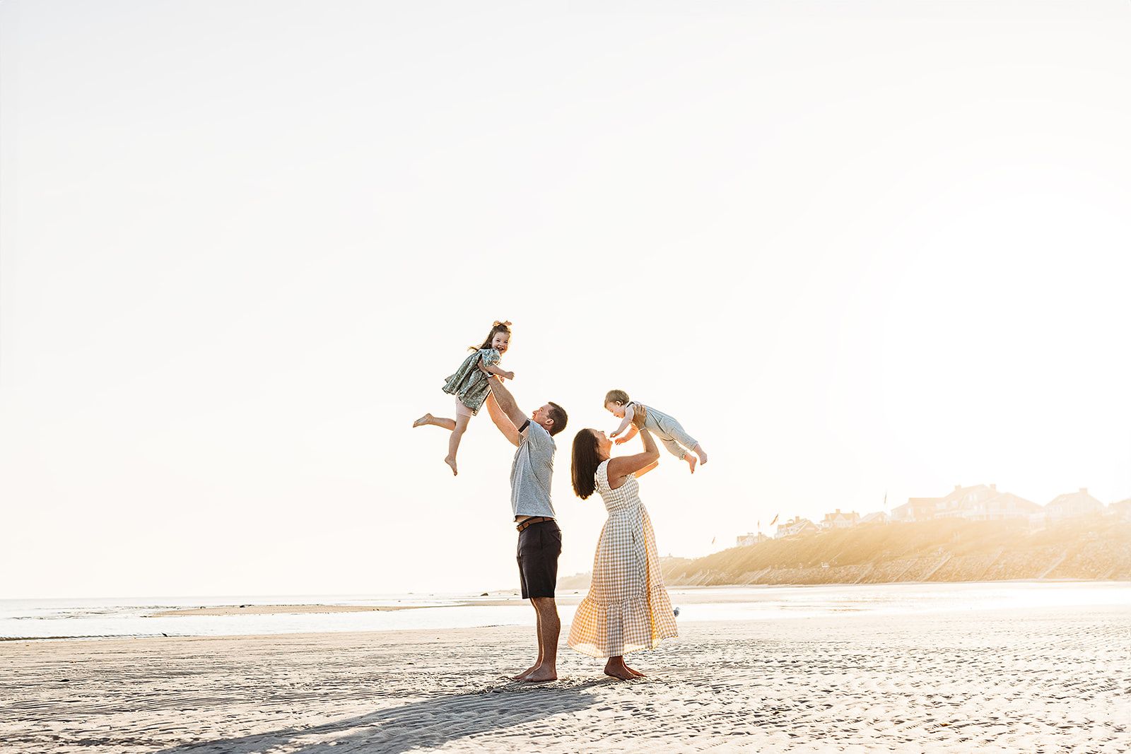A couple shares a romantic moment on a beach at sunset with mountains in the background.
