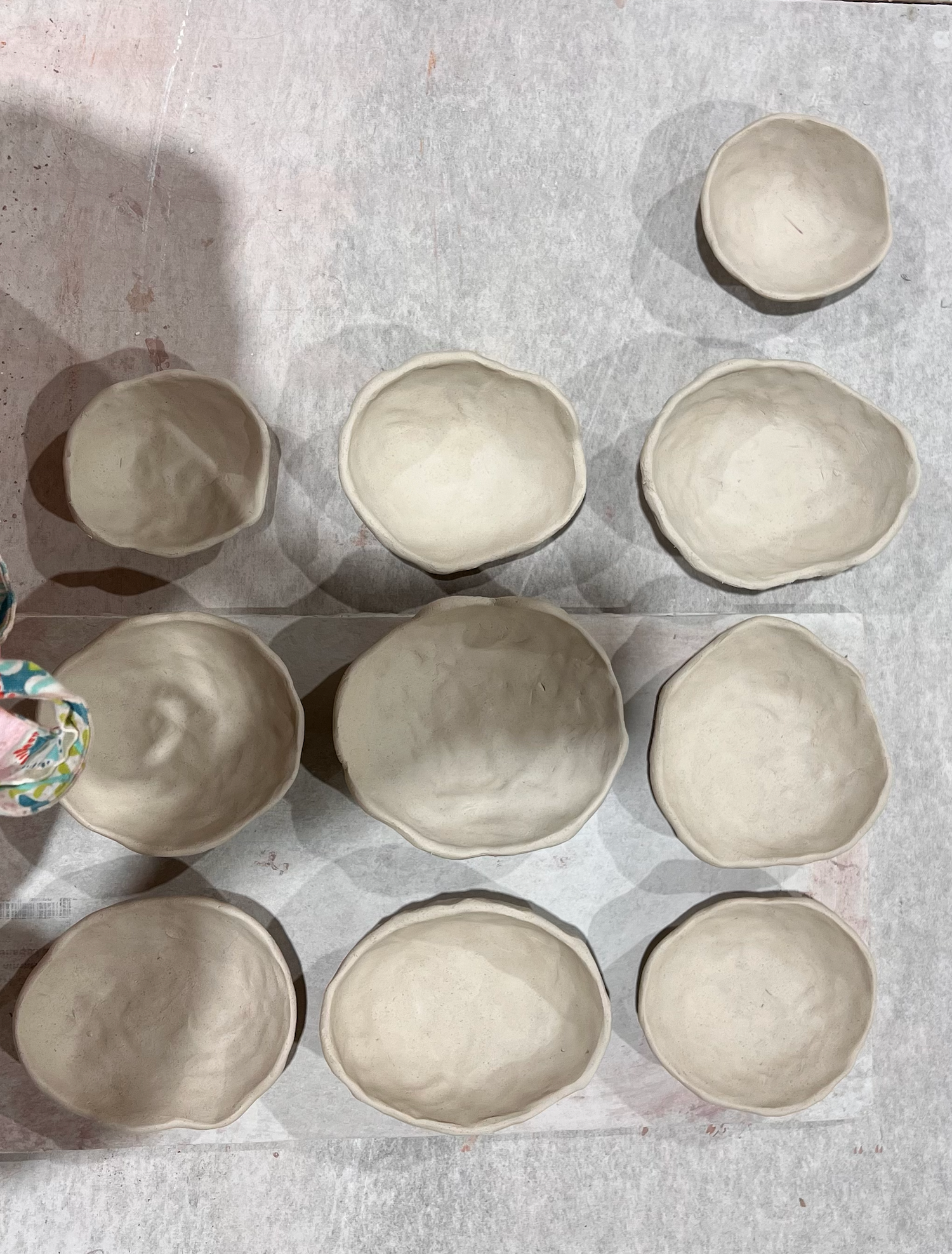 Nine unfired clay bowls of various sizes arranged on a work surface in a pottery studio.