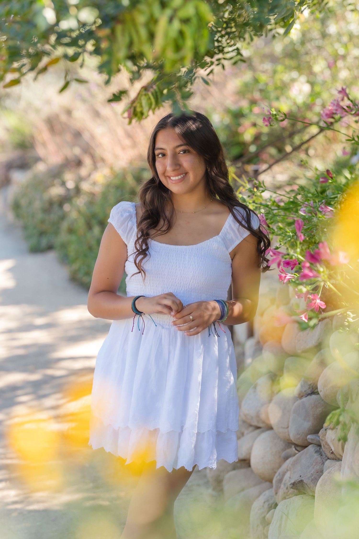 Summer portrait in a white dress among blooming garden flowers and greenery.
