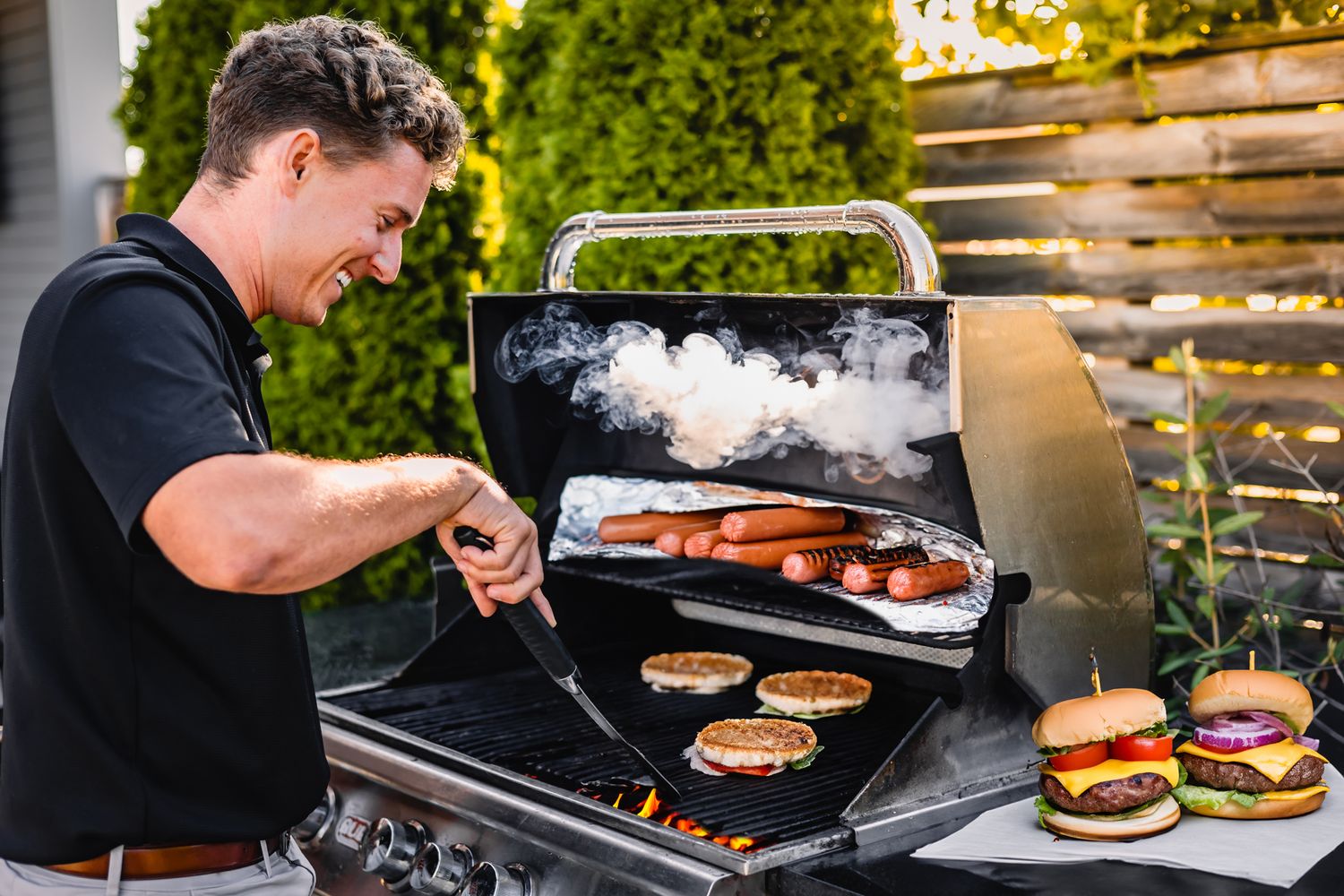 Person grilling burgers and hot dogs on outdoor barbecue grill.