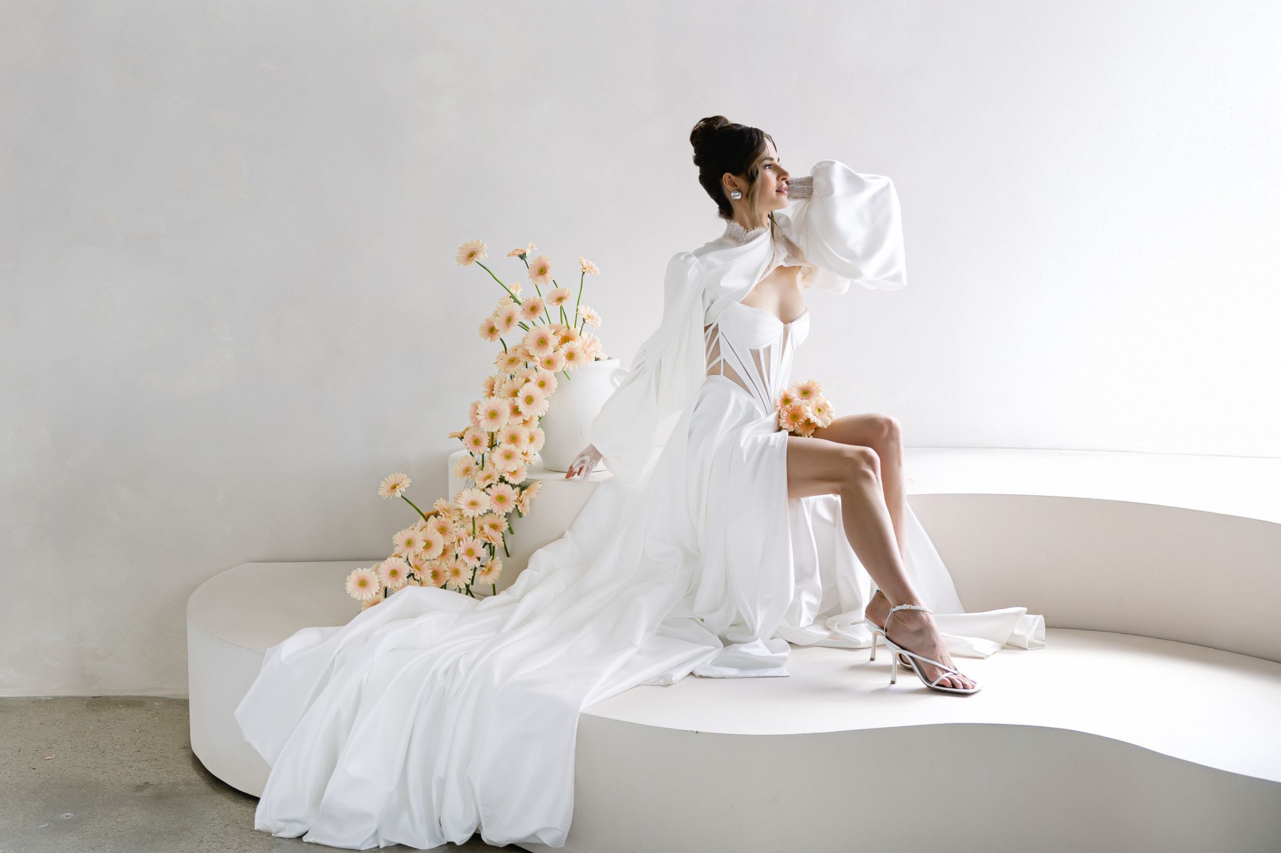 A person in a white flowing dress poses gracefully in a minimalist modern interior space.