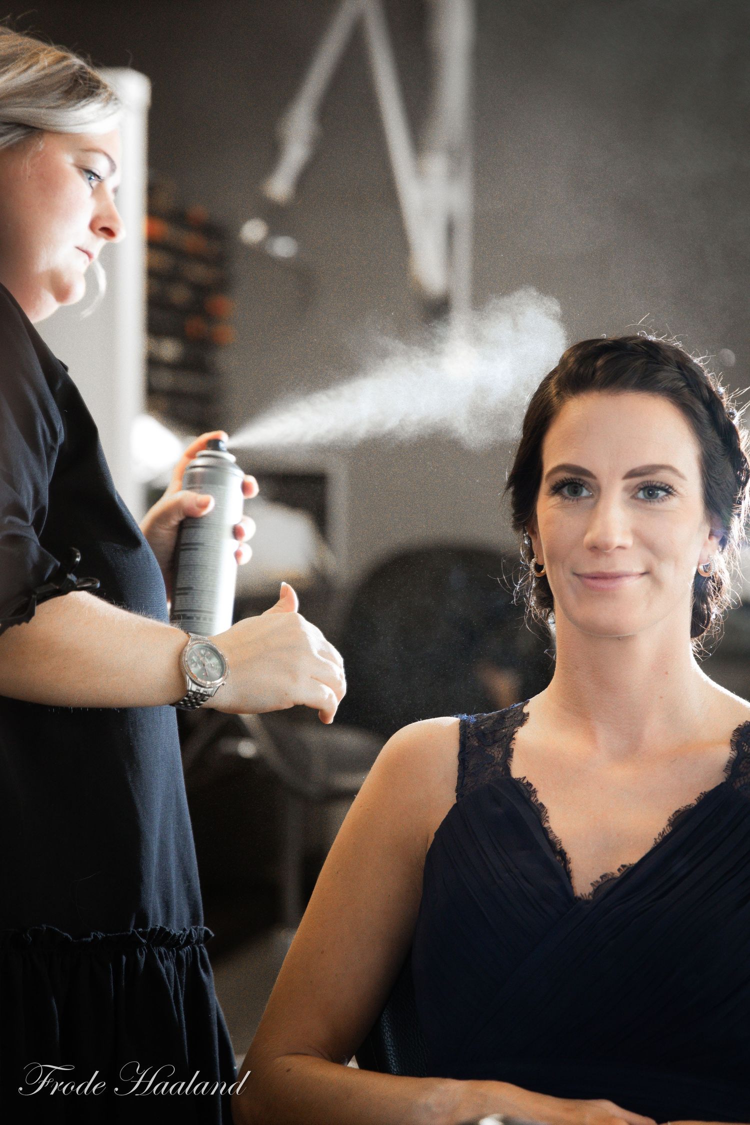 Hair stylist applying hairspray to brunette bride during wedding preparation in salon.