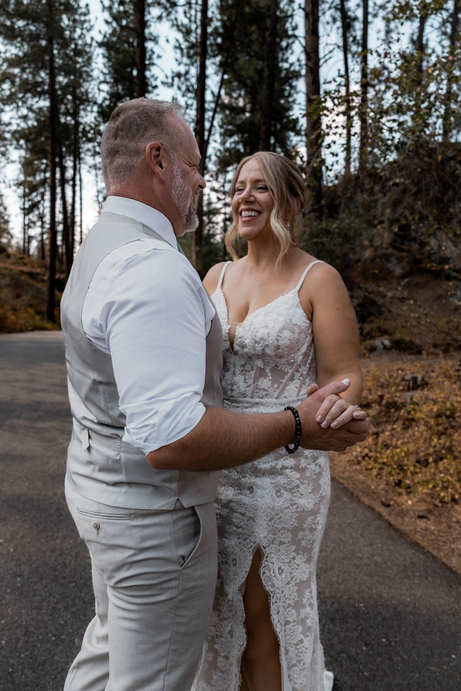 Couple sharing joyful moment on paved path with forest backdrop. Spokane wedding photographer.