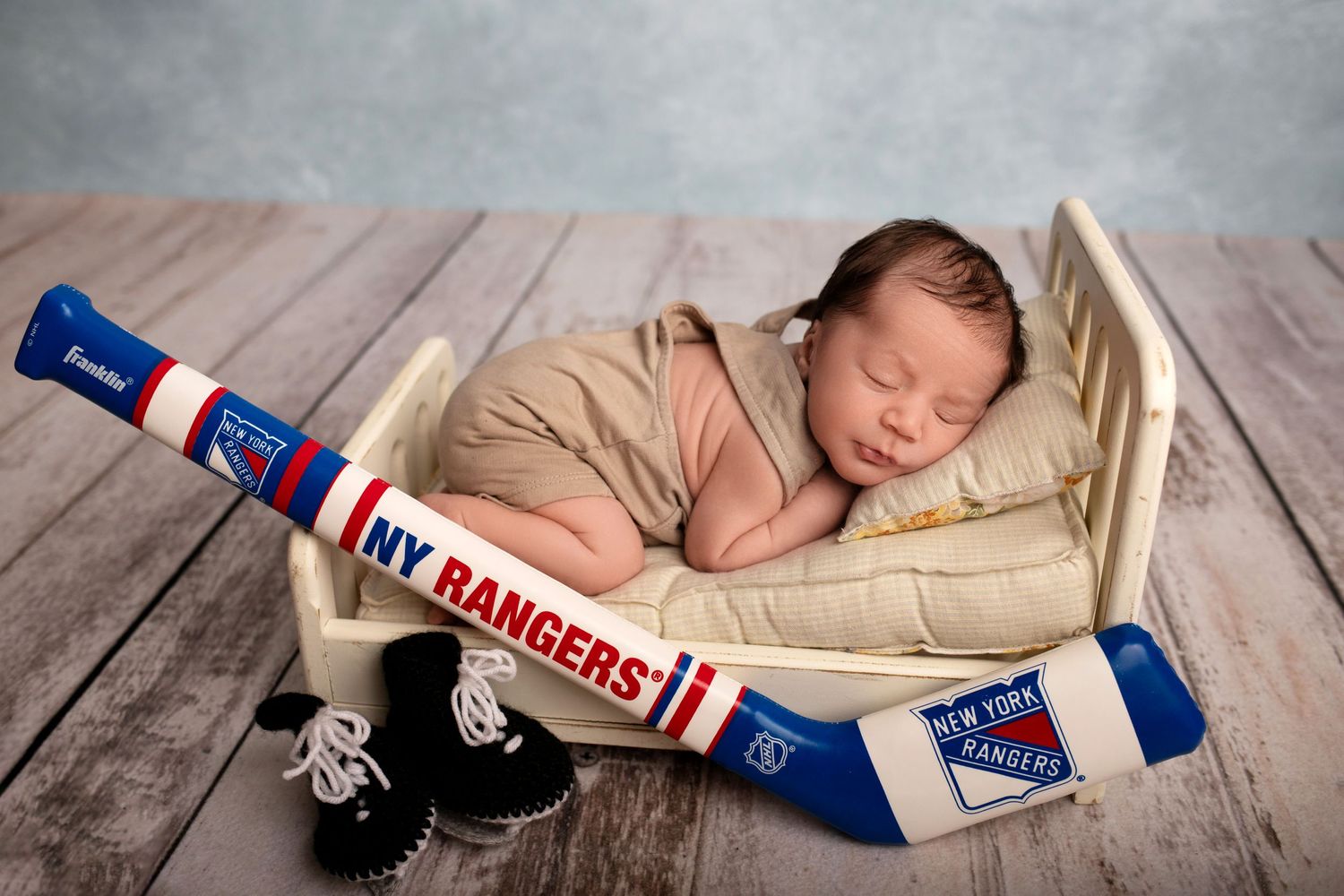 Sleeping newborn posed with NY Rangers hockey memorabilia on wooden floor.