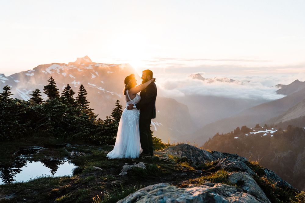 Wedding couple embracing on a mountain summit at golden sunset above the clouds.