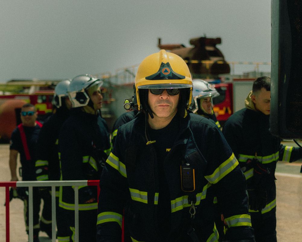 Firefighter in yellow helmet and protective gear stands at attention during emergency response training.