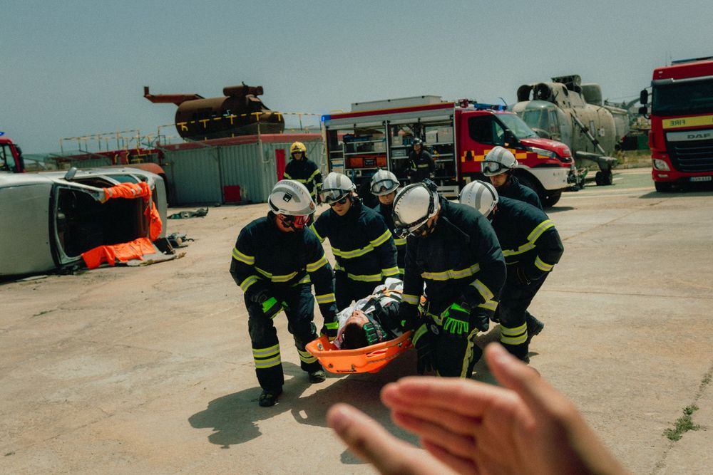 Team of firefighters in protective gear carry orange rescue equipment during training exercise.