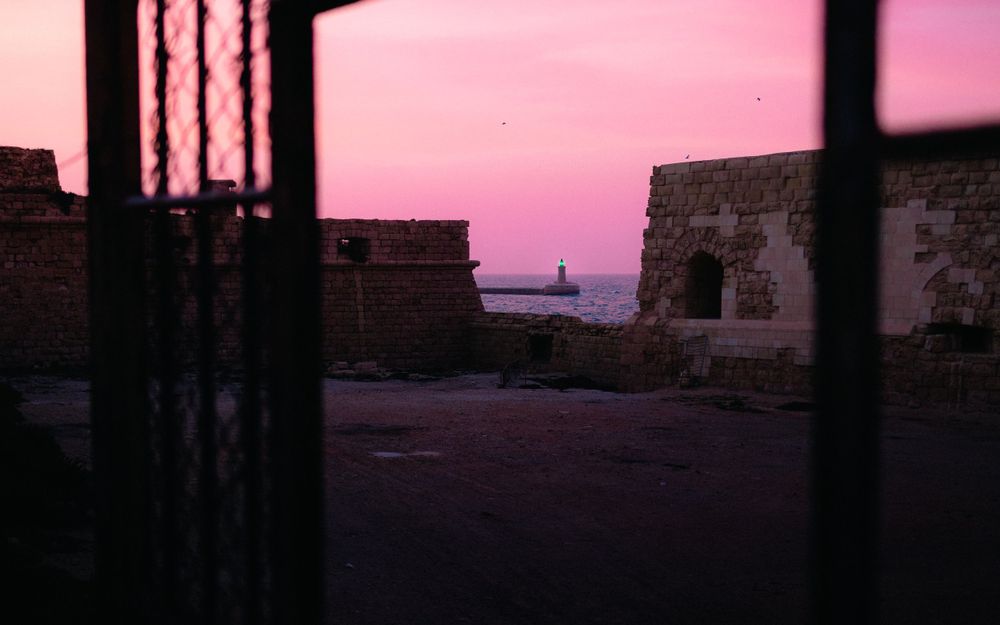 Pink sunset sky viewed through window bars with brick wall silhouette.