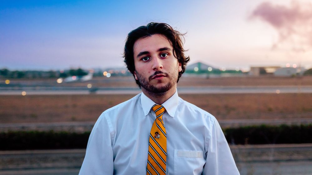 Portrait of a person wearing a white shirt and striped tie at an airport during sunset.
