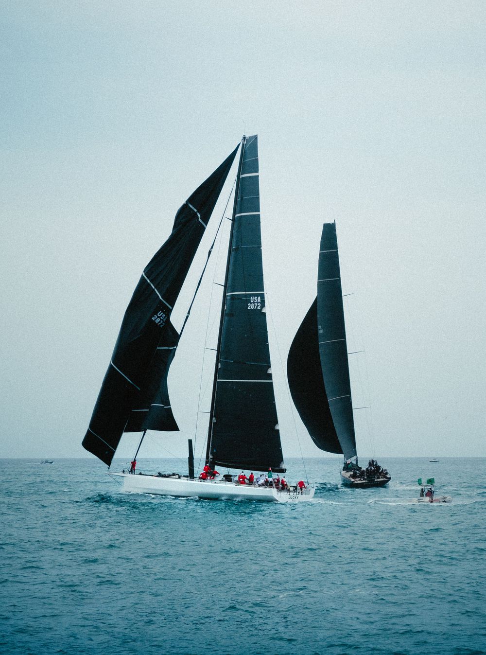 Racing sailboat with black sails cutting through ocean waters during a competition.
