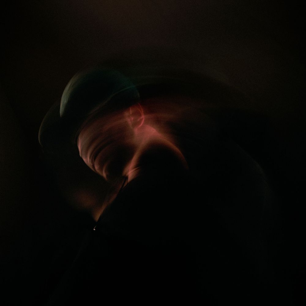 Dark atmospheric portrait with glowing orange light illuminating silhouette against black background.