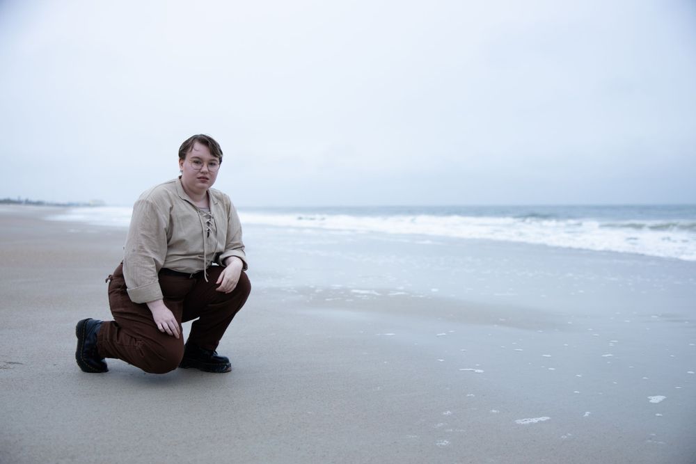 A figure crouches on a misty beach with waves and ocean in the background.
