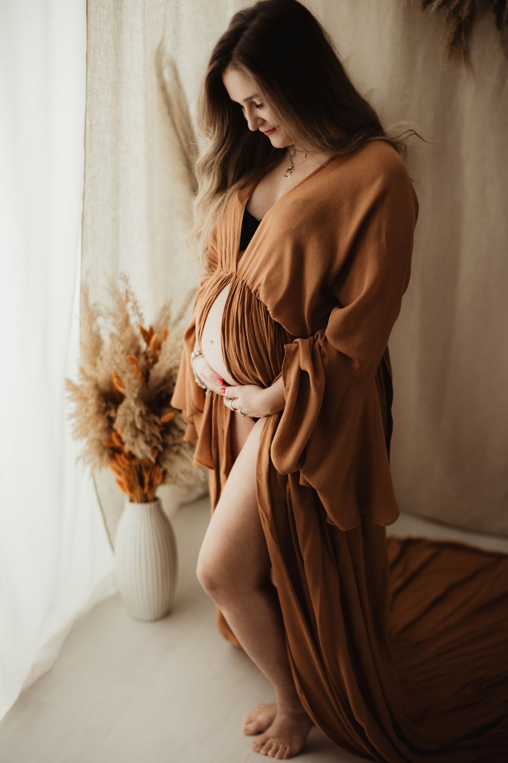 A series of maternity photos showing an expectant mother in a flowing brown dress against a light curtained backdrop.