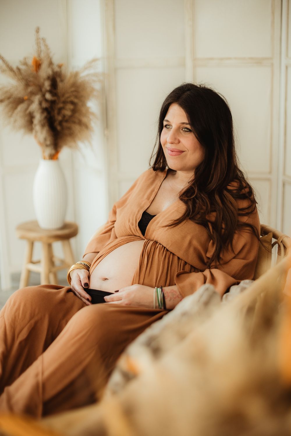 A woman in a brown dress sits comfortably on a couch in a bright, minimalist room with dried pampas grass decor.
