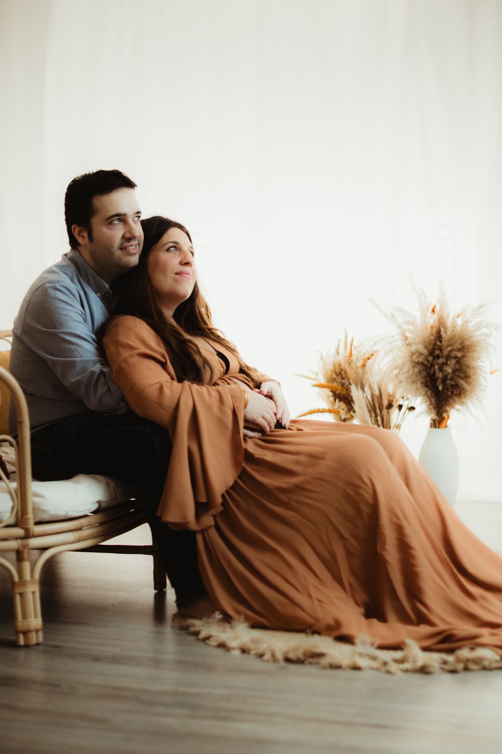 A couple in casual attire relaxes together on a hardwood floor with dried pampas grass decor in the background.