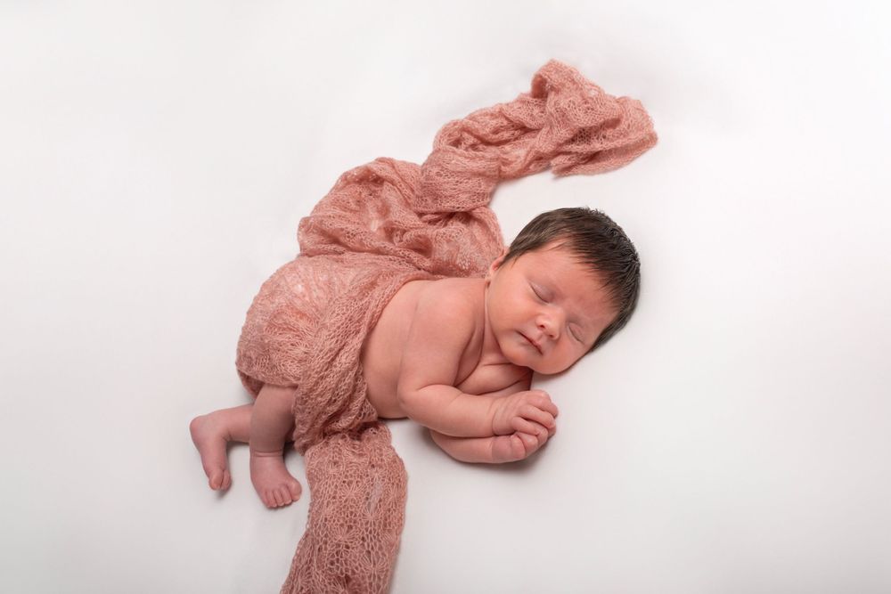 Newborn girl side pose on beanbag with soft pink wrap — newborn photography near Devizes