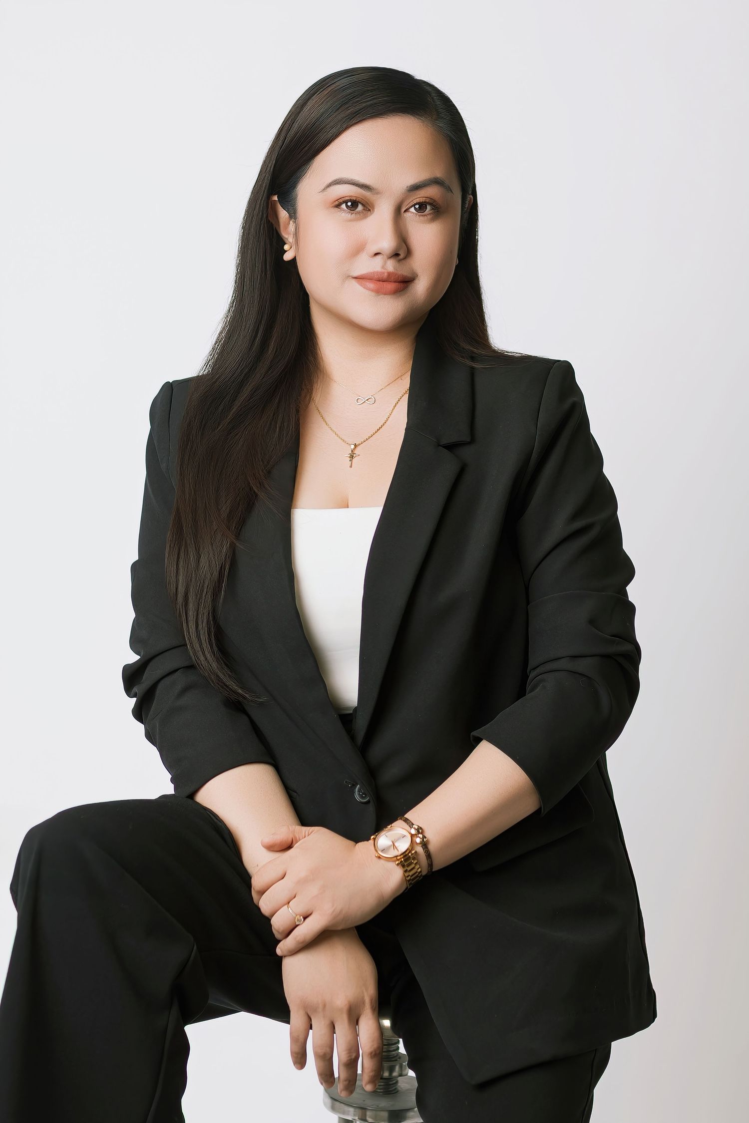 Professional portrait against white background showing person in black blazer and white top with long dark hair and jewelry.