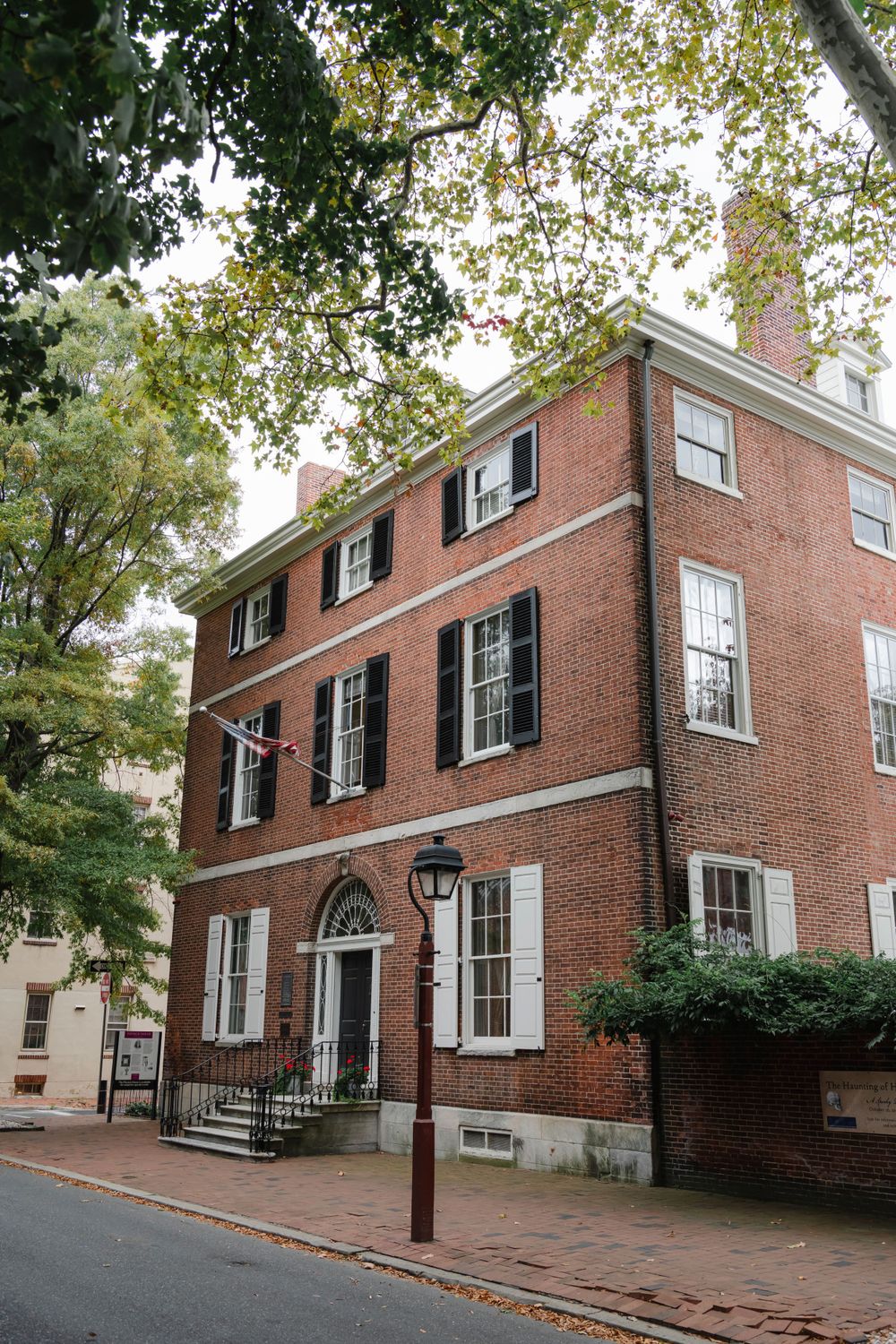 Historic red brick townhouse with black shutters and white trim on a tree-lined Philadelphia street.