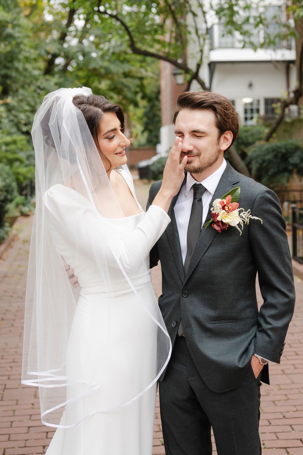 A joyful couple shares a tender moment of the bride wiping a tear from her groom on their wedding day outside on a brick pathway.
