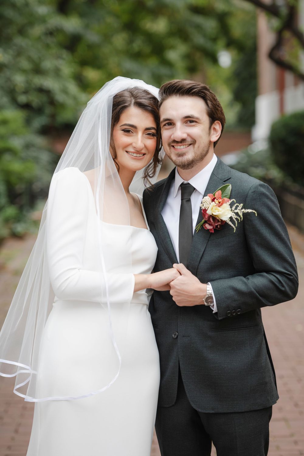 Elegant wedding couple poses on brick path with bride in white dress and veil, groom in black suit.