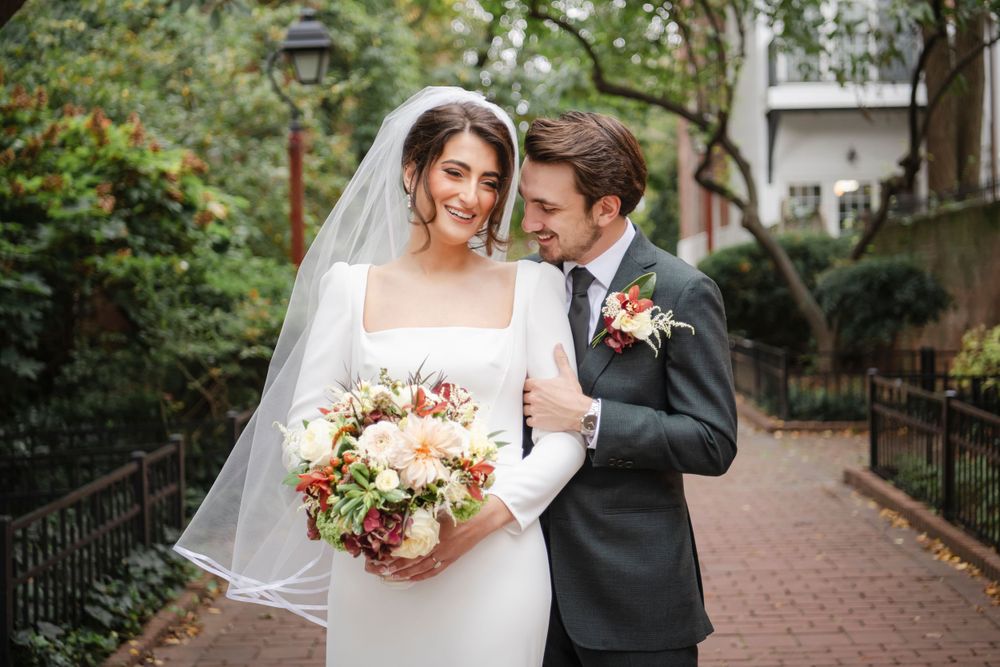 A happy couple shares an intimate moment on a brick pathway with an elegant bouquet and antique lamp post.