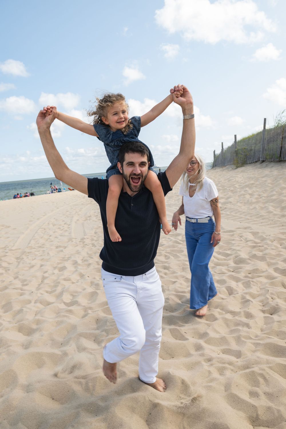 Two people play together on a sandy beach, jumping and holding hands on a sunny summer day.